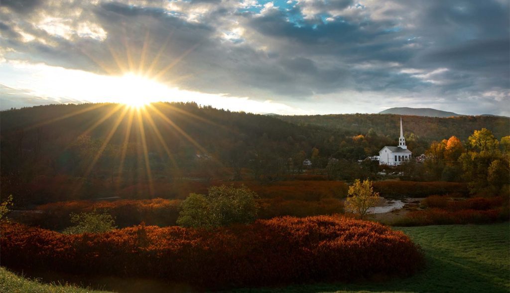 Autumn New England landscape with clouds, setting sun an white church with tall steeple.