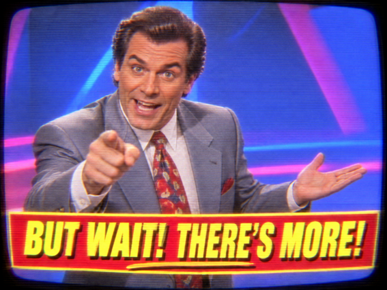 A retro 1990s late-night infomercial host in a grey suit pointing at the camera with one hand and gesturing with the other, above a bright yellow-on-red caption that reads BUT WAIT! THERE'S MORE!
